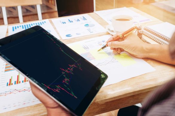 Un trader analyse des graphiques boursiers sur une tablette et prend des notes manuellement pour compléter son journal de trading