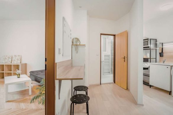Un appartement moderne et épuré avec un coin bureau en bois, des tabourets noirs et une cuisine ouverte pour réussir une décoration chaleureuse.