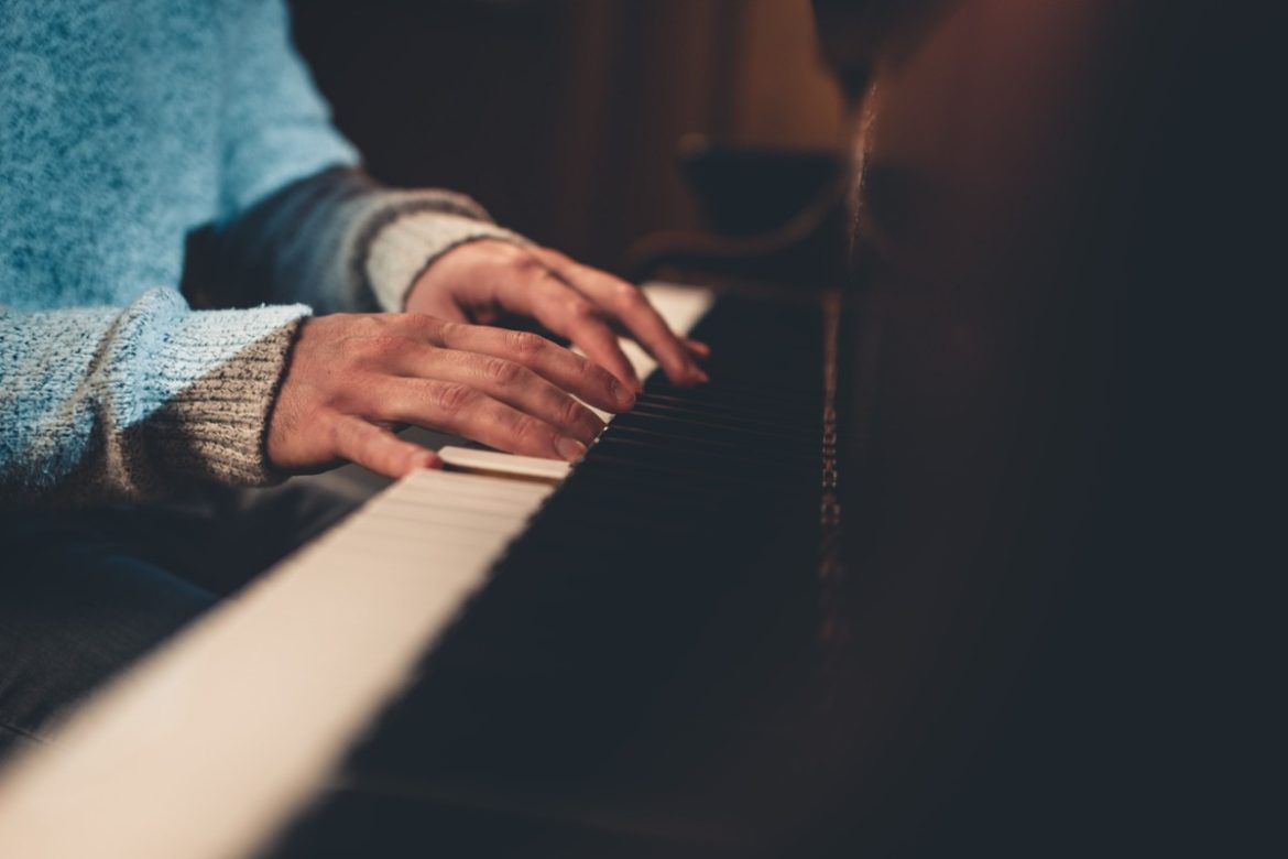 Deux mains matures portant un pull tricoté doux sont positionnées sur le clavier d'un grand piano à queue sombre, une étude attentive pour les pianistes débutants adultes