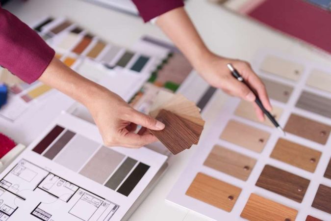 Une architecte d'intérieur utilise des nuanciers de couleurs et des échantillons de bois sur un plan de maison pour son projet optimisé par l'IA.