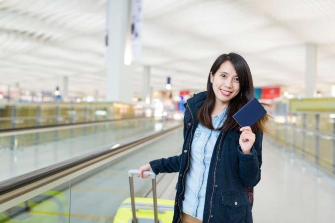 Une voyageuse souriante avec son passeport et sa valise, prête à partir en voyage depuis l'aéroport.