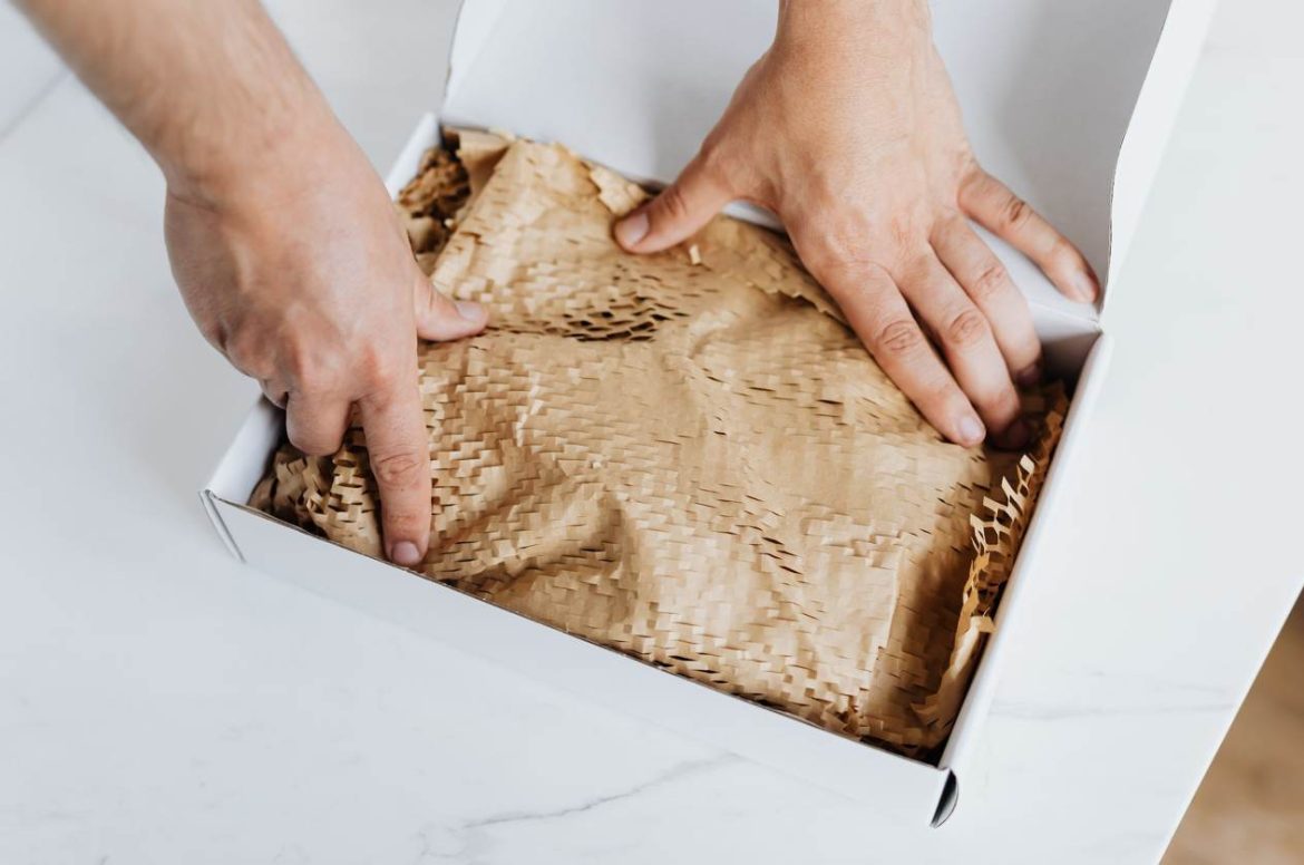 Deux mains installant du papier kraft nid d'abeille dans un carton pour montrer comment remplacer le papier bulle pour emballer du fragile.