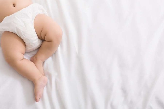 Gros plan sur le bas du corps d'un bébé en couche sur un drap blanc, idéal pour illustrer des conseils pour soulager la peau irritée.