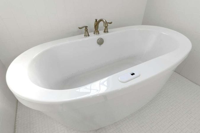 Vue plongeante sur une baignoire îlot ovale en céramique blanche, équipée d'une robinetterie dorée et d'un trop-plein moderne dans une salle de bains lumineuse.