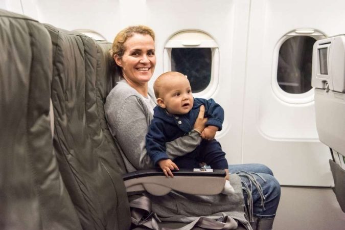 Une mère souriante tient son bébé dans ses bras à bord d'un avion, illustrant les déplacements lors d'un voyageur avec un bébé.